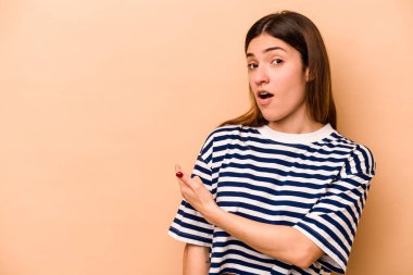 Latin kökenli genç bir kadın bej arka planda izole edilmiş gülümsüyor ve boş alanda bir şeyler gösteriyor..