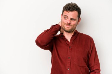 Beyaz arka planda izole edilmiş genç beyaz bir adam kafasının arkasına dokunuyor, düşünüyor ve bir seçim yapıyor..