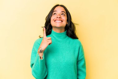 Sarı arka planda izole edilmiş genç İspanyol kadın iki parmağı da boş bir alan gösteriyor..