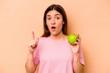 Bej arka planda izole edilmiş bir elma tutan genç İspanyol kadının bir fikri var, ilham verici bir kavram..