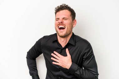 Beyaz arka planda soyutlanmış beyaz tenli genç bir adam gülüyor, elini yüreğine koyuyor, mutluluk kavramını koruyor..