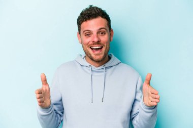 Mavi arka planda izole genç beyaz adam iki eliyle bir şey tutuyor, ürün sunumu..