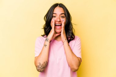 Latin kökenli genç bir kadın sarı arka planda izole edilmiş. Dedikodu yapıyor, bir şeyleri bildiriyor..