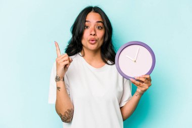 Mavi arka planda bir saat tutan genç İspanyol kadının harika bir fikri var, yaratıcılık kavramı..