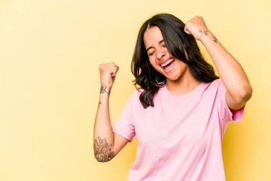 Sarı arka planda izole edilmiş genç İspanyol kadın zaferden sonra yumruk kaldırıyor, kazanan konsept..