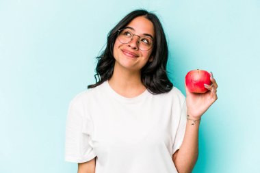Elma tutan genç İspanyol kadın mavi arka planda hedeflerine ve amaçlarına ulaşma hayali kuruyor.