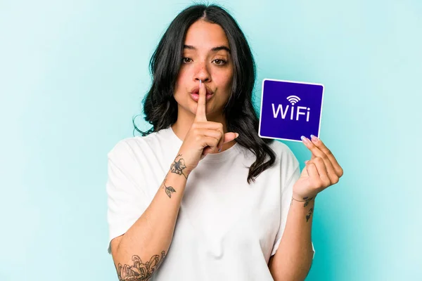 Young hispanic woman holding wifi placard isolated on yellow background keeping a secret or asking for silence.