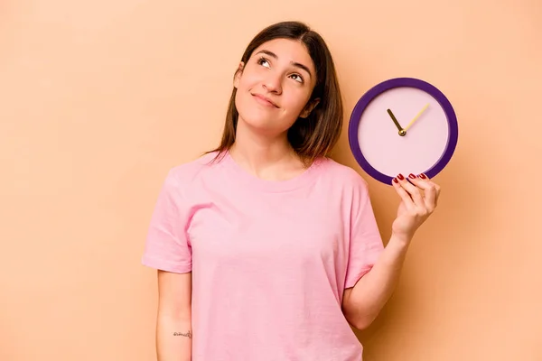 Joven Mujer Hispana Sosteniendo Reloj Aislado Sobre Fondo Beige Soñando — Foto de Stock