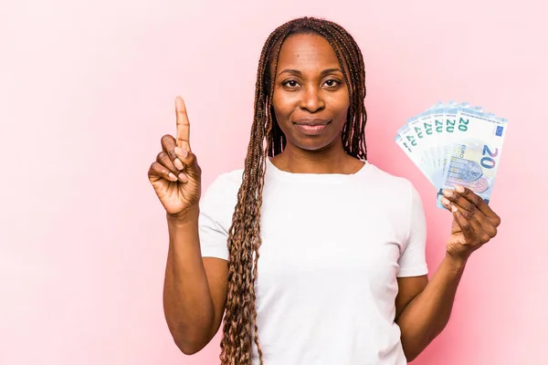 Mladá Afroameričanka Drží Bankovky Izolované Růžovém Pozadí Ukazující Číslo Jedna — Stock fotografie