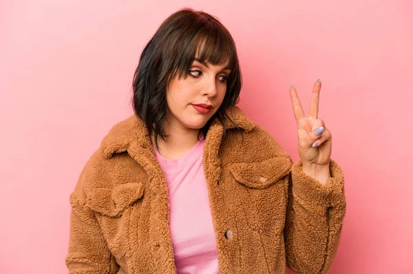 Genç beyaz kadın pembe arka planda izole edilmiş neşeli ve kaygısız parmakları olan bir barış sembolü gösteriyor..