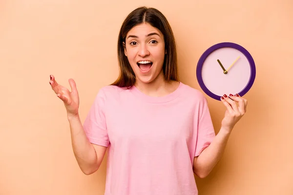 Mujer Hispana Joven Sosteniendo Reloj Aislado Sobre Fondo Beige Recibiendo — Foto de Stock