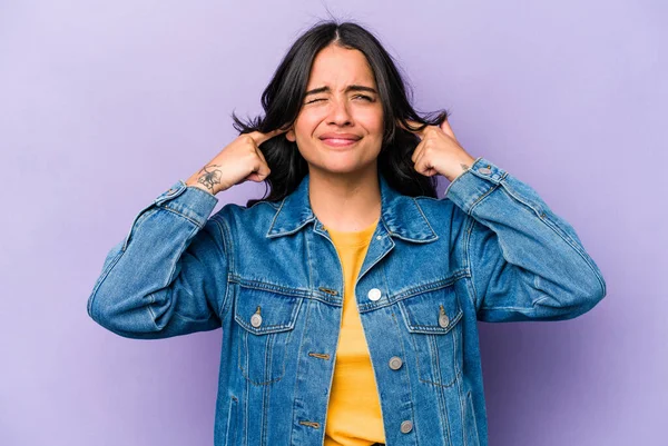 Mor arka planda izole edilmiş, parmaklarıyla kulaklarını kapatan, gürültülü bir ortam tarafından stresli ve çaresiz genç İspanyol kadın..