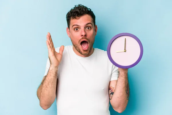 Joven Hombre Caucásico Sosteniendo Reloj Aislado Sobre Fondo Azul Sorprendido — Foto de Stock