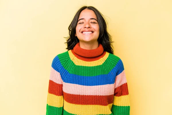 Sarı arka planda izole edilmiş genç İspanyol kadın gülüyor ve gözlerini kapıyor, rahatlamış ve mutlu hissediyor..