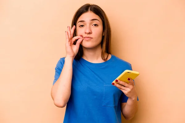 Młoda Kaukaska Kobieta Trzyma Telefon Komórkowy Odizolowany Beżowym Tle Palcami — Zdjęcie stockowe