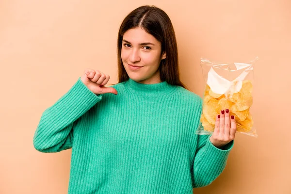 Bej arka planda izole edilmiş bir paket cipsi tutan genç İspanyol kadın gururlu ve kendinden emin hissediyor, örnek olarak.