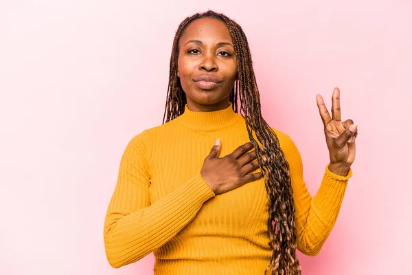 Genç Afrikalı Amerikalı kadın pembe arka planda izole edilmiş yemin ediyor, elini göğsüne koyuyor..