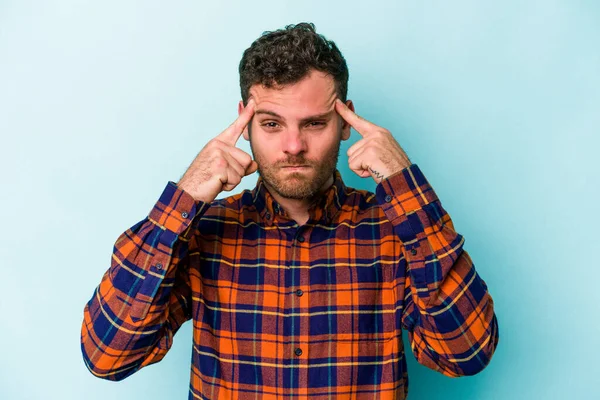 Kafkasyalı genç adam mavi arka planda izole edilmiş bir göreve odaklanmış, parmaklarını işaret ediyor..