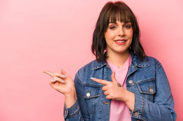 Pembe arka planda izole edilmiş genç beyaz kadın işaret parmaklarıyla işaret ederek heyecanlanıyor..
