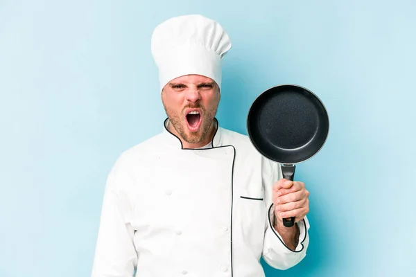 年轻的高加索厨师拿着一只被蓝色背景隔离的飞盘大喊大叫 非常愤怒和好斗 — 图库照片