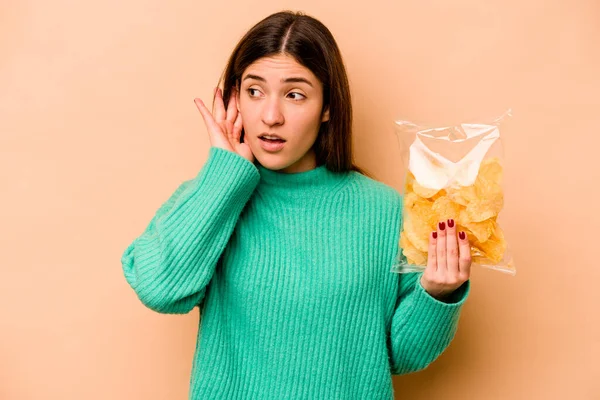 年轻的惊慌失措的女人手里拿着一袋因米黄色背景而被隔离的薯片 想听一些闲话 — 图库照片