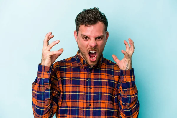 Mavi arka planda izole edilmiş genç beyaz adam öfkeyle bağırıyor..