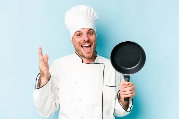 年轻的高加索厨师拿着被蓝色背景隔离的飞盘 带着惊喜 兴奋地举起双手 — 图库照片