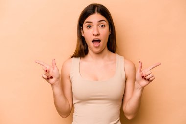 Latin kökenli genç bir kadın bej arka planda izole edilmiş. Farklı kopya alanlarını gösteriyor. Birini seçiyor, parmaklarıyla gösteriyor..