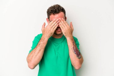 Beyaz arka planda izole edilmiş genç beyaz bir adam elleriyle gözlerini kapatmaktan korkuyor..