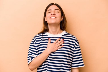 Latin kökenli genç bir kadın, bej arka planda izole edilmiş. Kahkahalar atıyor..