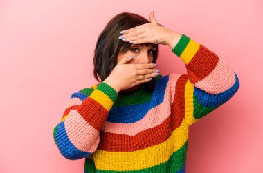 Pembe arka planda izole edilmiş genç beyaz kadın kameraya parmaklarıyla göz kırpıyor, yüzünü kapatmaktan utanıyor..