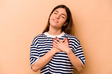 Bej arka planda izole edilmiş genç İspanyol kadın, avuçlarını göğsüne bastıran dostça bir ifadeye sahip. Aşk konsepti.