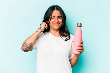 Mavi arka planda termo tutan genç İspanyol kadın kulaklarını elleriyle kapatıyor..