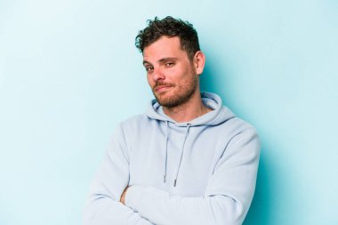 Mavi arka planda izole edilmiş genç beyaz adam alaycı bir ifadeyle kameraya bakarken mutsuz oluyor..