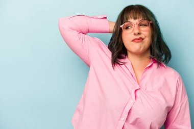 Kafkasyalı genç bir kadın mavi arka planda izole edilmiş kafasının arkasına dokunuyor, düşünüyor ve bir seçim yapıyor..