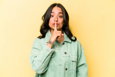 Sarı arka planda izole edilmiş genç İspanyol kadın ya sır saklıyor ya da sessizlik istiyor..