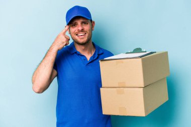 Mavi arka planda izole edilmiş genç beyaz teslimatçı işaret parmağıyla hayal kırıklığı jesti gösteriyor..