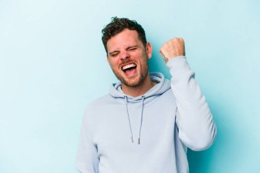 Mavi arka planda izole edilmiş genç beyaz bir adam zaferi, tutkuyu ve coşkuyu kutluyor, mutlu bir ifade..