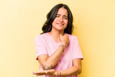 Genç İspanyol kadın sarı arka planda izole edilmiş, dirsek masajı yapıyor, kötü bir hareketin ardından acı çekiyor..