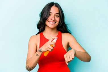 Mavi arka planda güneş kremi tutan genç İspanyol kadın.