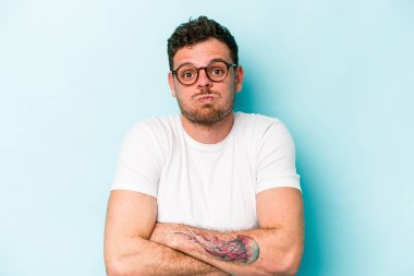 Mavi arka planda izole edilmiş genç beyaz adamın yanakları şişer, yorgun bir ifadesi vardır. Yüz ifadesi kavramı.