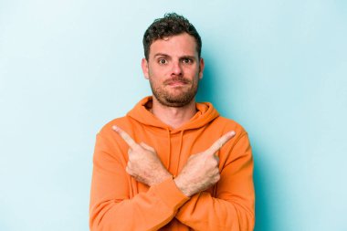 Mavi arka plan noktalarında izole genç beyaz adam, iki seçenek arasında seçim yapmaya çalışıyor.