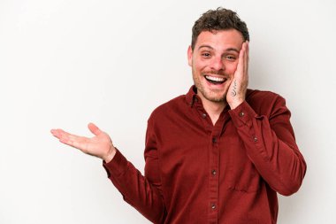 Beyaz arka planda izole edilmiş genç beyaz bir adam bir avuç içinde fotokopi alanı tutuyor, el üstünde tutuyor. Şaşırmış ve mutlu..