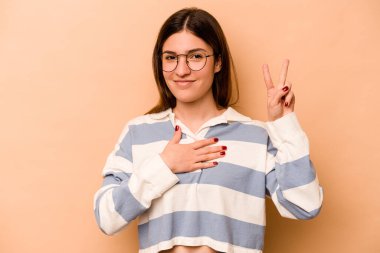 Genç İspanyol kadın bej arka planda izole edilmiş yemin ediyor, elini göğsüne koyuyor..