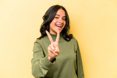 Sarı arka planda izole edilmiş genç İspanyol kadın iki numarayı parmaklarıyla gösteriyor..