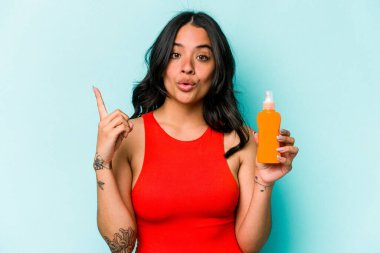 Mavi arka planda güneş kremi tutan genç İspanyol kadının harika bir fikri var, yaratıcılık kavramı..