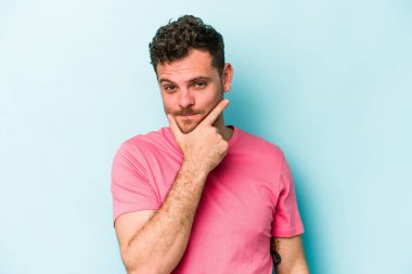 Kafkasyalı genç bir adam mavi arka planda izole edilmiş. Bir strateji planlıyor, bir iş yolu düşünüyor..