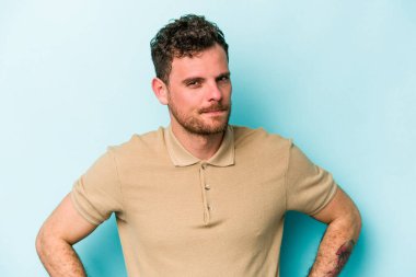 Kafkasyalı genç adam mavi arka planda izole, kafası karışmış, şüpheli ve güvensiz hissediyor..