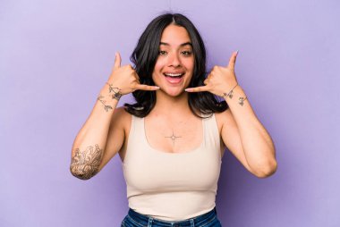 Mor arka planda izole edilmiş genç İspanyol kadın parmaklarıyla bir cep telefonu hareketi gösteriyor..