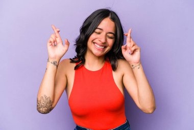 Mor arka planda izole edilmiş genç İspanyol kadın şans dilemek için parmaklarını çapraz yapıyor.